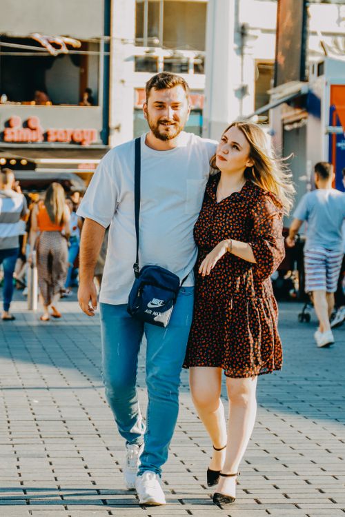Free A young couple walking arm in arm down a bustling city street on a sunny day. Stock Photo
