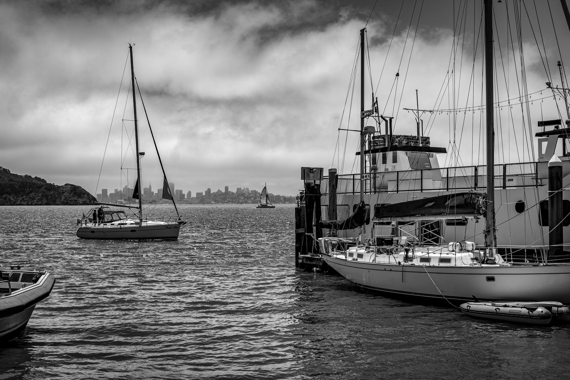 Dramatic black and white photo of sailboats moored in a harbor with city skyline overcast.