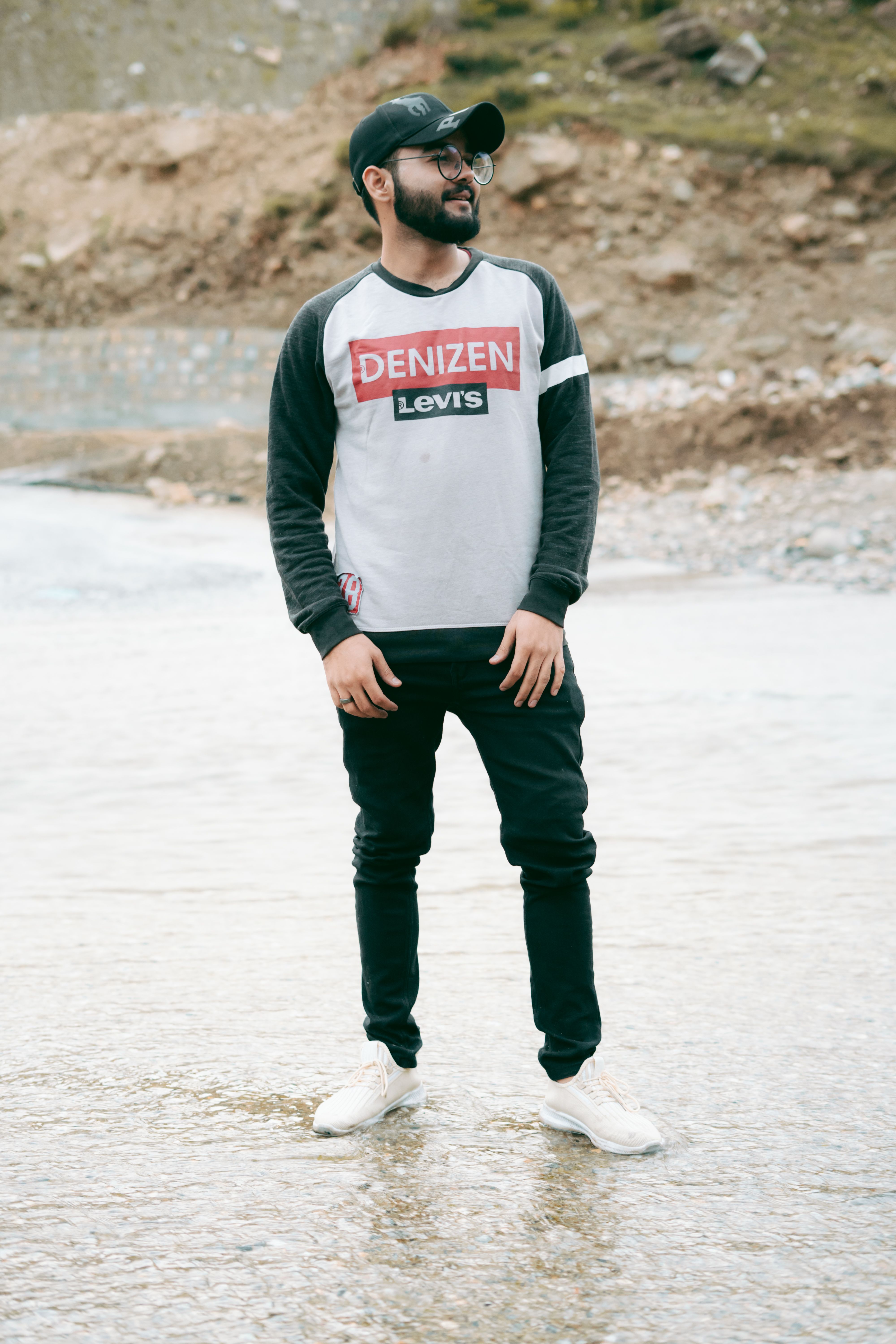 Young man wearing casual attire stands by a rocky stream, showcasing relaxed style.