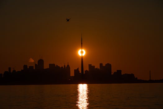 Beautiful sunset view of Toronto skyline with CN Tower, capturing the silhouette against a warm orange sky.