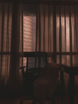 Silhouette of a chair against a softly lit window in a moody dark room.