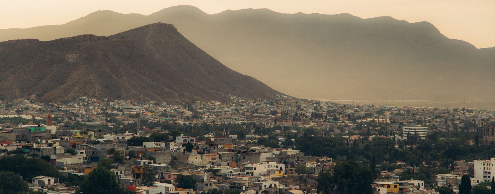 A serene aerial view of a city nestled at the base of a mountain, captured during a hazy dusk.