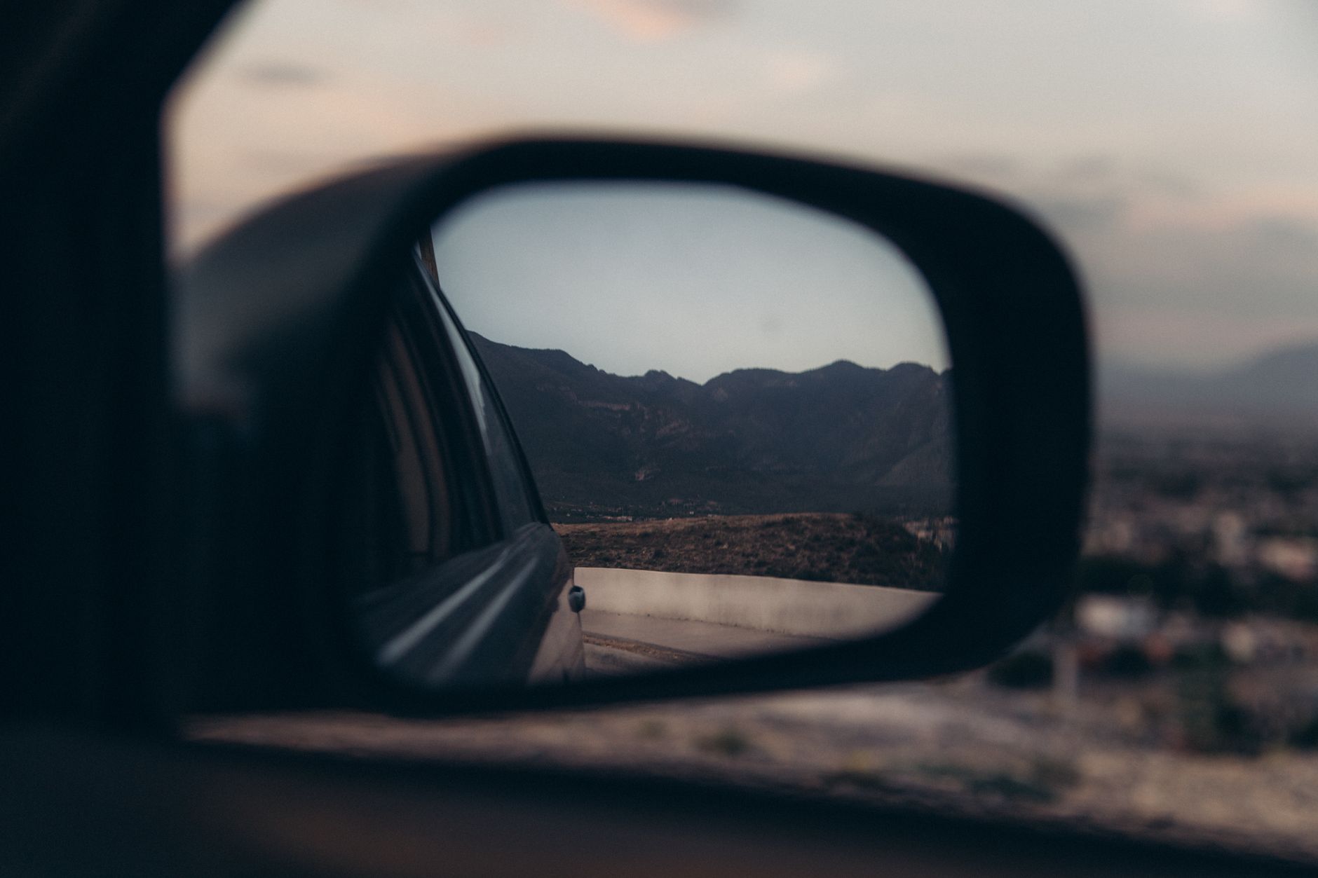 A scenic mountain view reflected in a car side mirror during twilight, showcasing serene natural beauty.