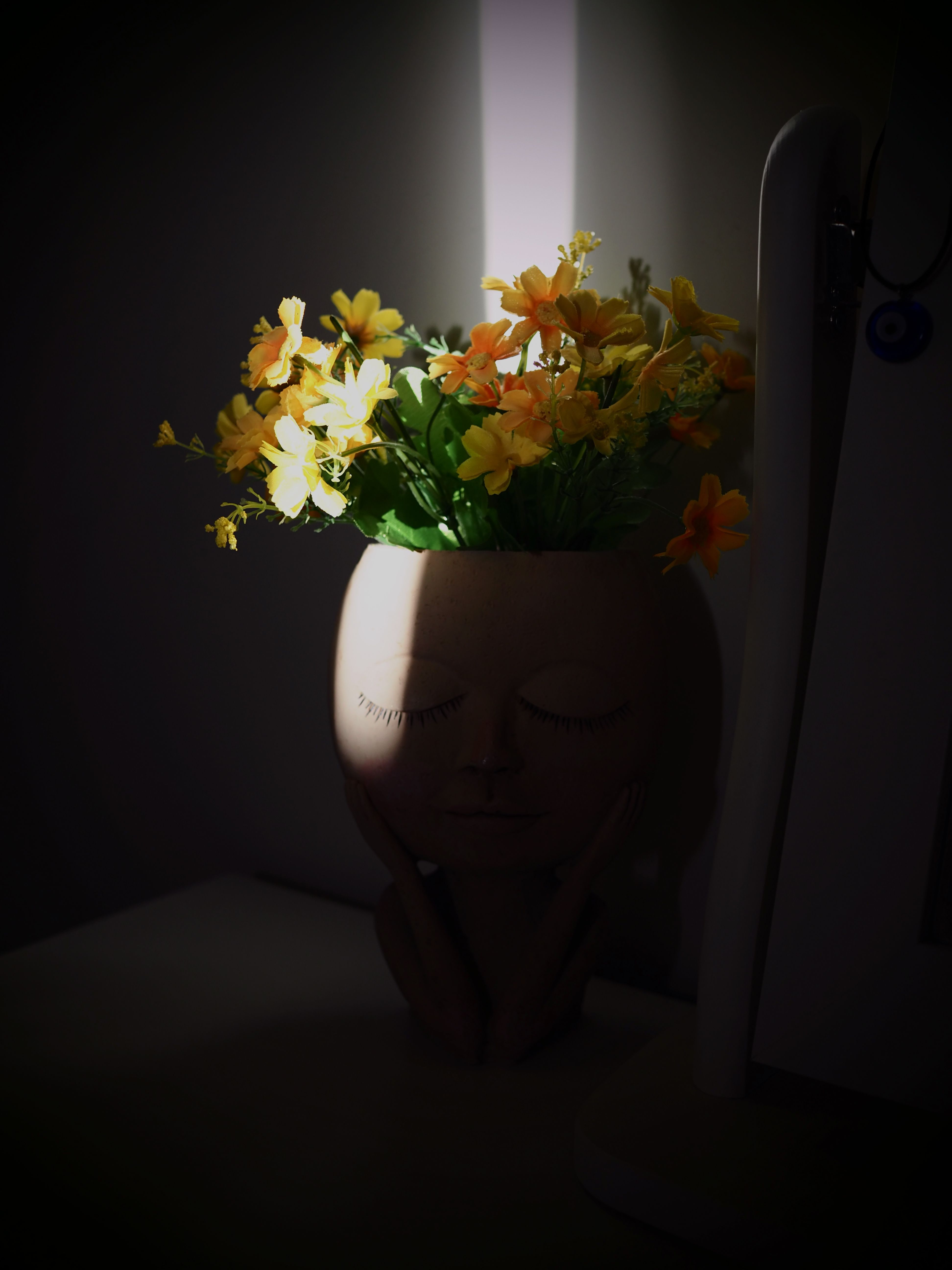 Yellow and orange flowers in a face-shaped vase, beautifully lit in a dark room.
