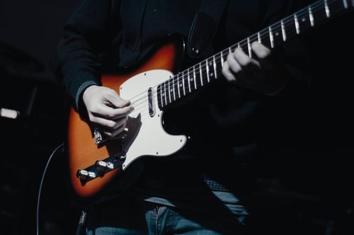 Free A musician plays an electric guitar with precision in dim lighting, emphasizing musical focus. Stock Photo
