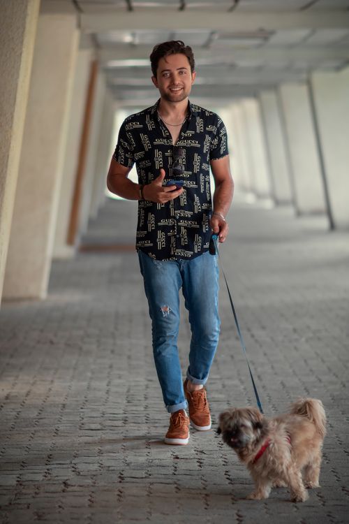 Free Smiling young man in casual attire walking his dog in an outdoor corridor. Stock Photo