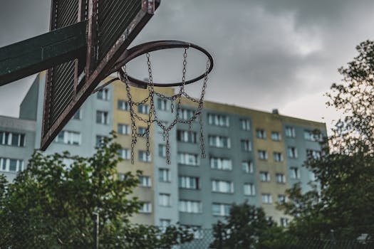 Rusty basketball hoop in a Gdańsk neighborhood with residential buildings on a cloudy day.