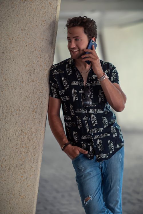 Free A fashionable man smiles while talking on the phone, leaning against a wall. Stock Photo