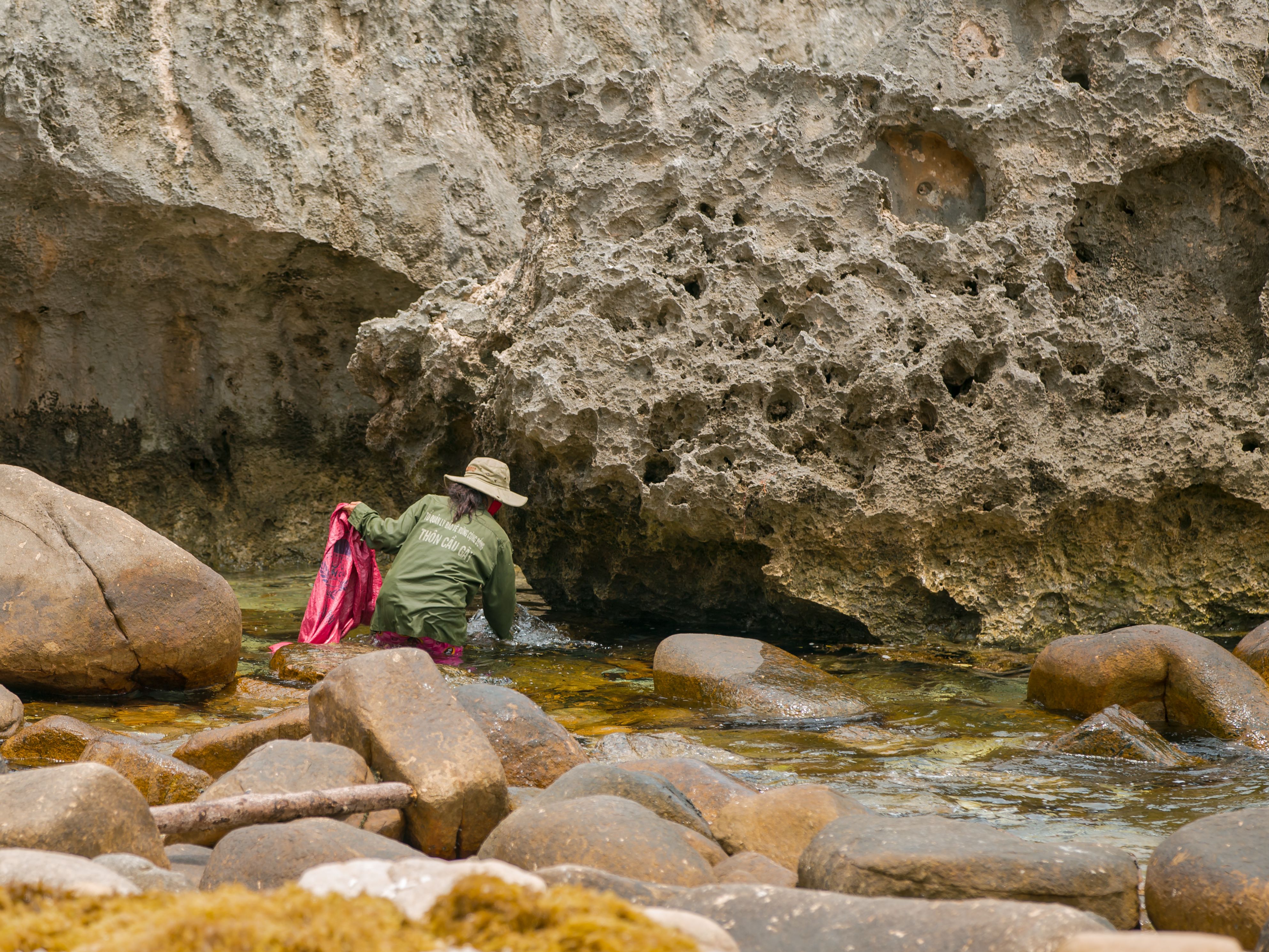 Individual exploring rocky shoreline with unique formations and clear water. Captured outdoors during daytime.