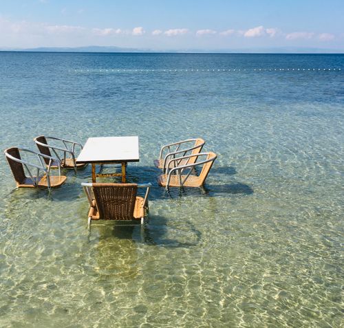 Free Chairs and table set in shallow crystal clear ocean water, Erdek, Türkiye. Stock Photo
