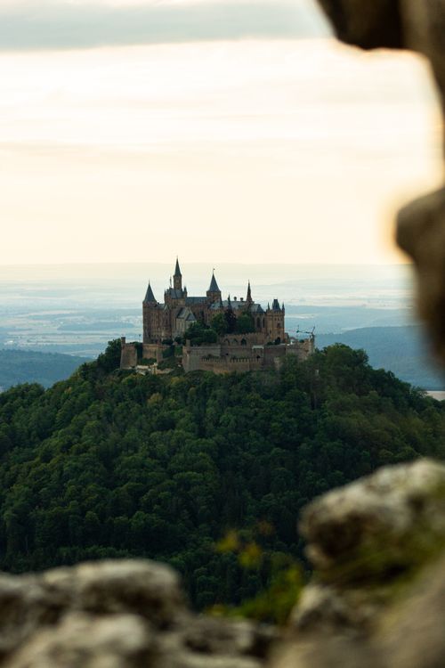 Free A majestic view of Hohenzollern Castle set against a serene sunset, perched on a lush hilltop. Stock Photo