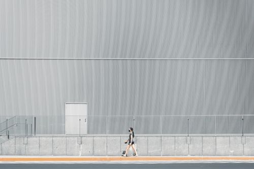 Free Woman walks along a modern minimalist urban building. Stylish and simplistic street scene. Stock Photo