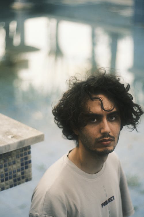 Young Man with Messy Hair and a Stubble Standing by the Pool 