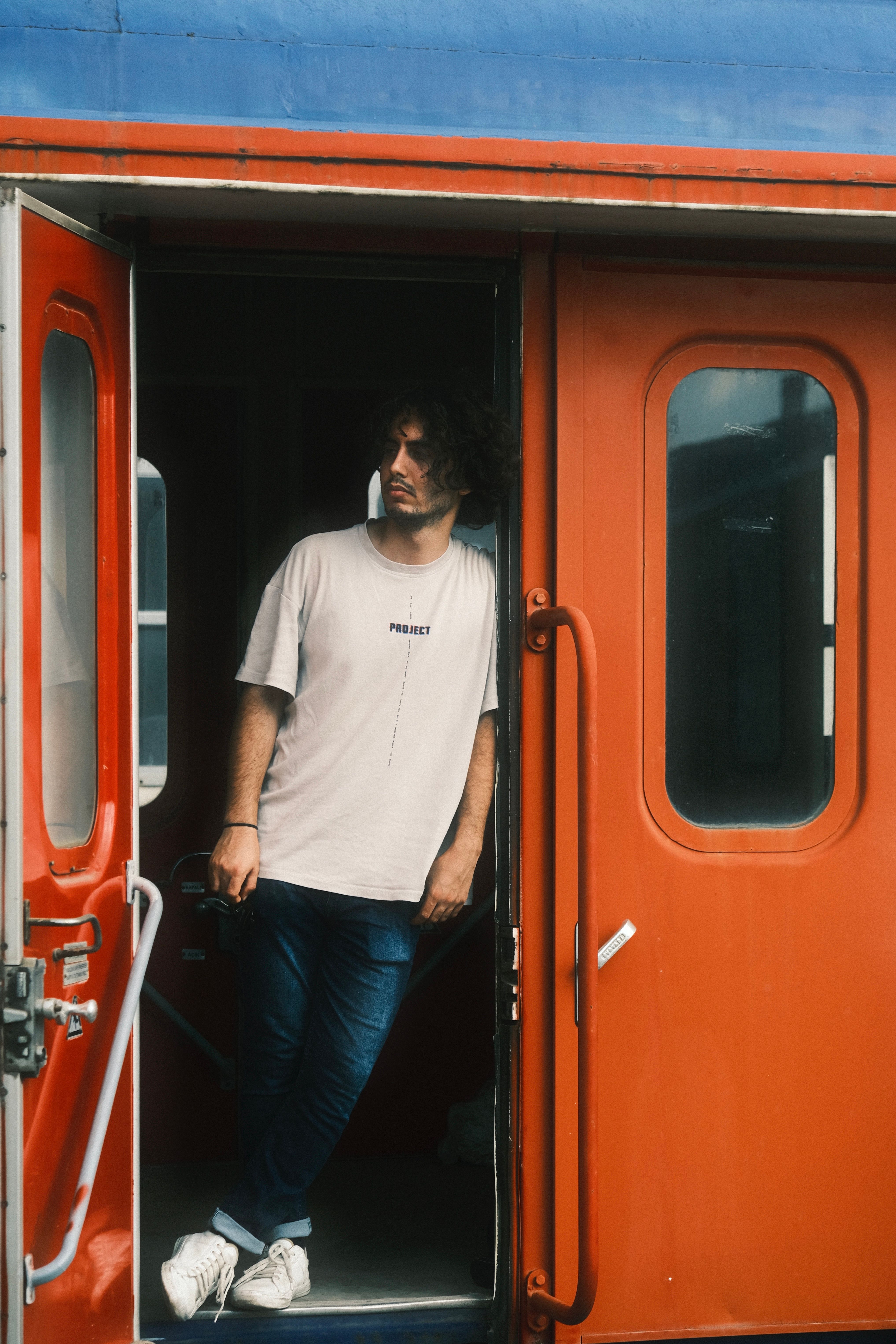 Casually dressed man leans in a vibrant train doorway, creating a relaxed travel vibe.