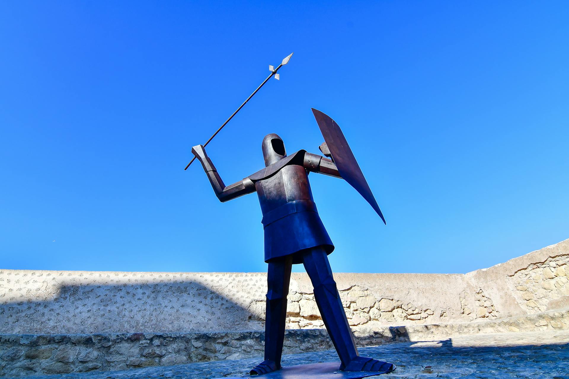 A captivating knight statue wielding a spear and shield against a clear blue sky in Alicante, Spain.