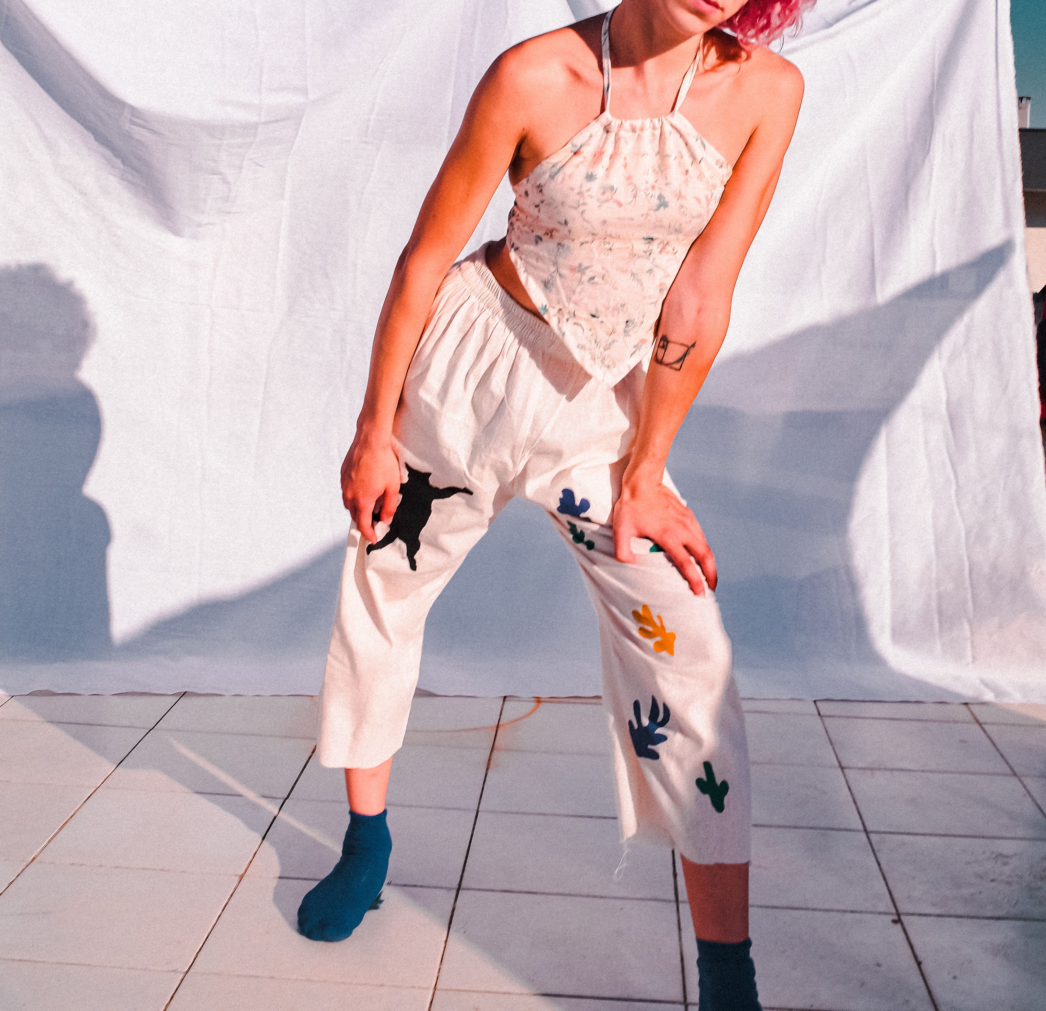 Stylish outdoor portrait of a woman in artistic clothing posing against a white backdrop.
