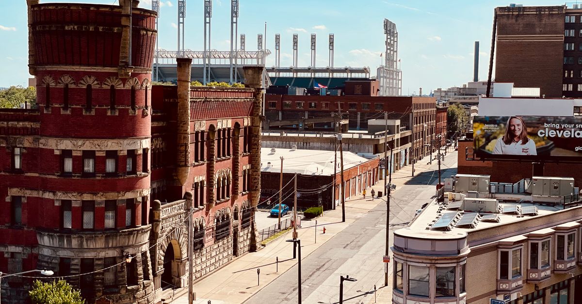 A sunny urban scene in Cleveland featuring the historic Grays Armory and a distant baseball stadium.