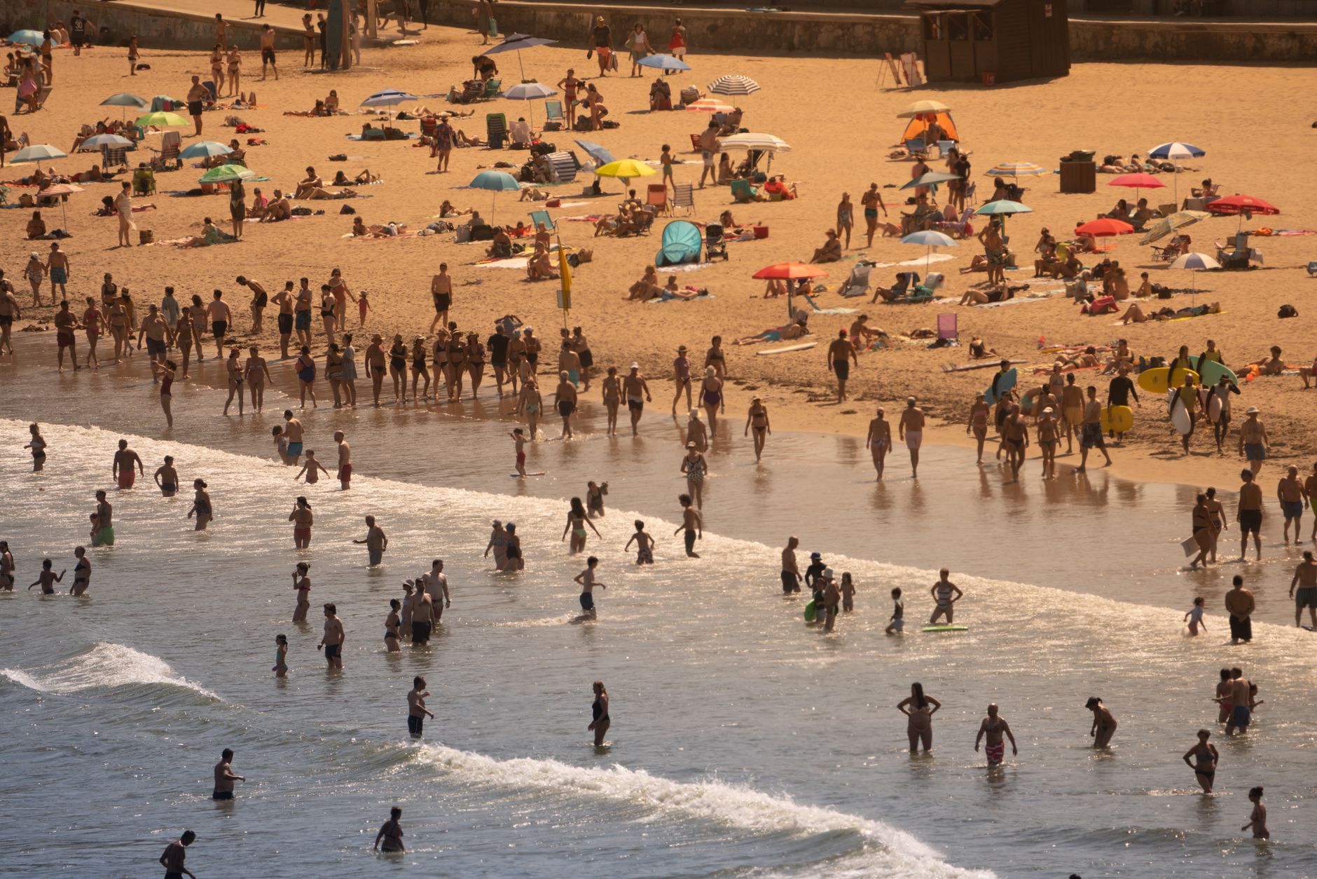 Vista aérea de una playa concurrida con personas disfrutando de un soleado día de verano.