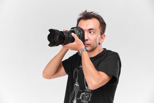 Portrait of a male photographer capturing an image with a professional camera against a plain white backdrop.