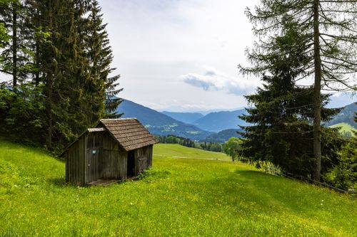 Free Charming rural scene featuring a cabin in a lush mountainous landscape under a cloudy sky. Stock Photo