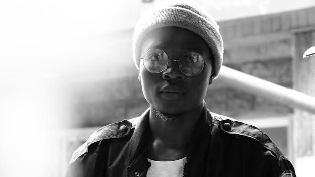 户外，一名戴着眼镜和无檐帽的年轻人黑白肖像