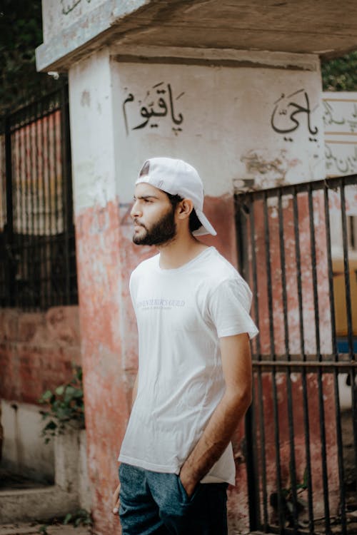 Man in White  T-shirt and White Cap Standing Near a Gate 