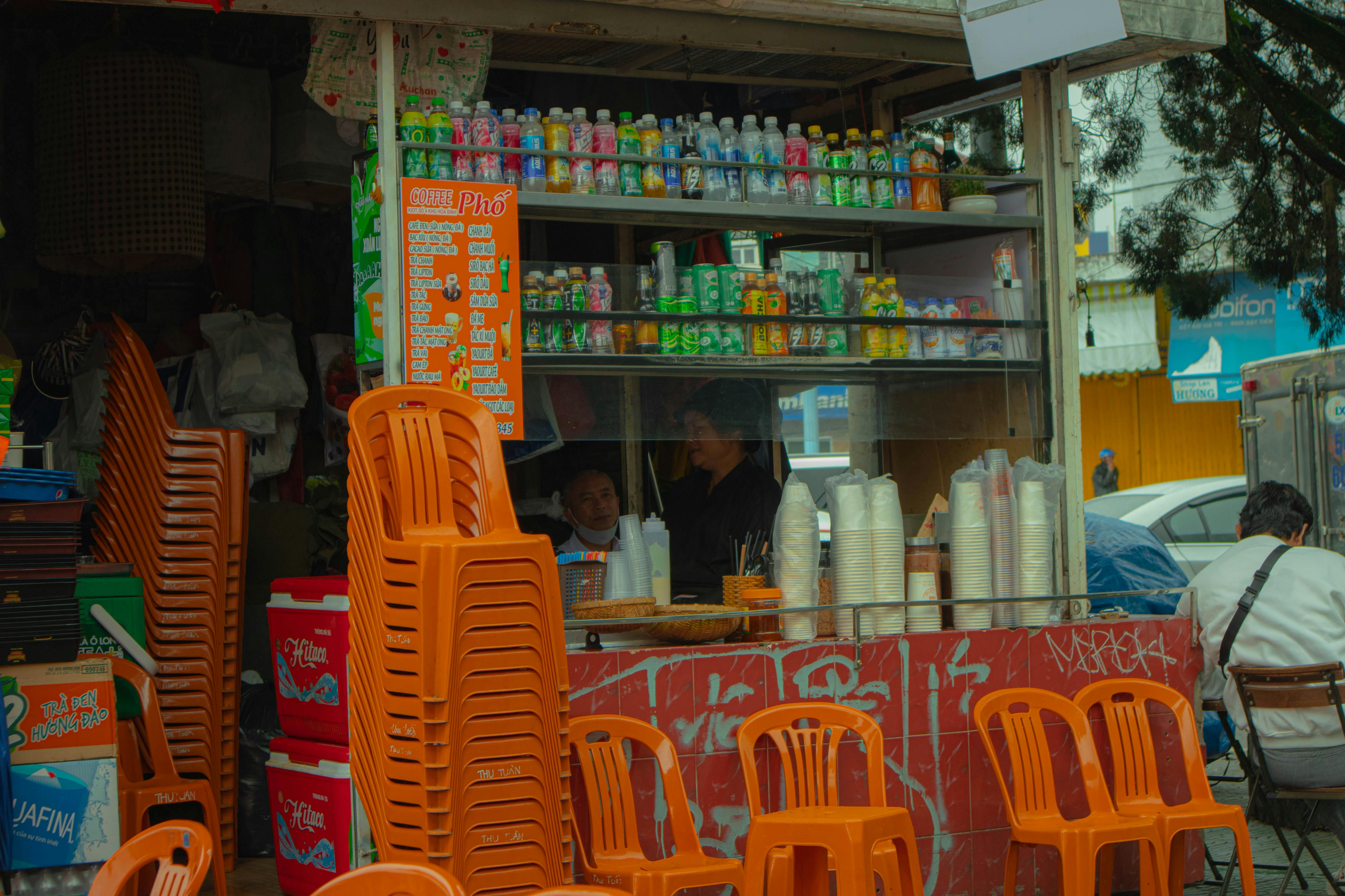 Colorful street food stall in Dalat with stacked chairs and drink displays.