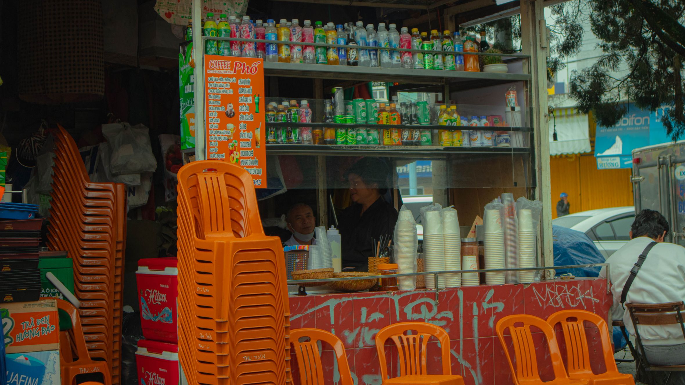 Colorful street food stall in Dalat with stacked chairs and drink displays.