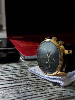 Elegant gold wristwatch placed on a stylish wooden surface with a laptop in the background.