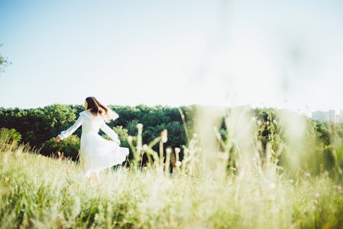 Woman in White Dress Walking on Green Grass Field