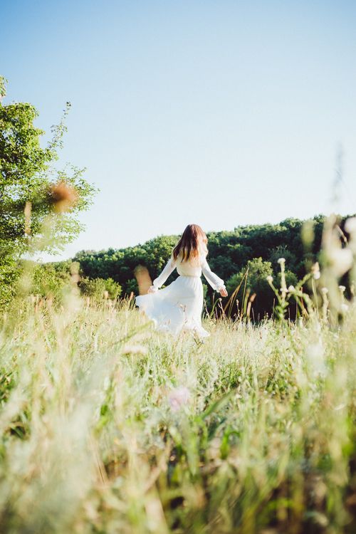 Free A serene view of a woman in a white dress standing in a summer meadow. Stock Photo
