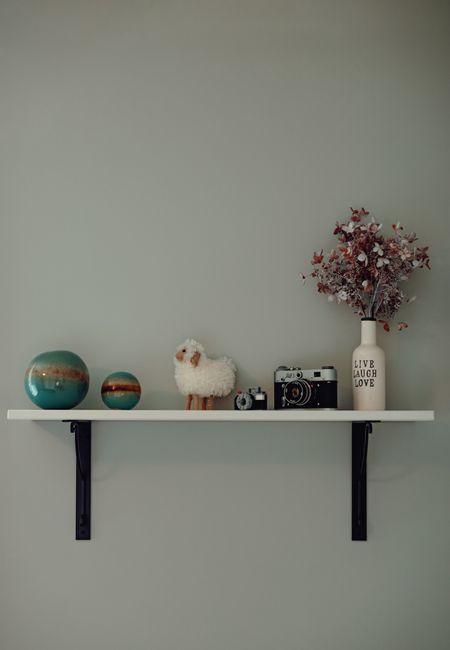 A minimalist shelf with decor items including a vintage camera, vase with flowers, and decorative spheres.