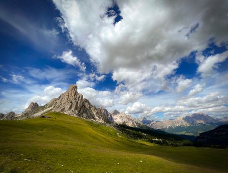 A breathtaking view of a mountain range with lush meadows and dramatic clouds in the sky.