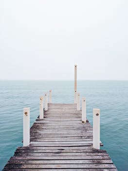 A tranquil view of a wooden pier extending into a calm, expansive lake under a clear sky. Perfect for nature lovers.