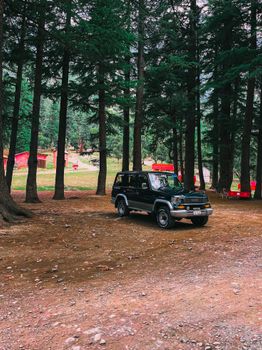 An SUV is parked in a serene forest camping area with tall trees around, ideal for outdoors travel.