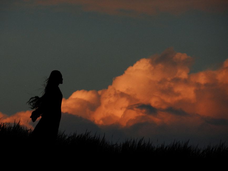 Silhouette of a woman against a vibrant sunset sky with dramatic clouds, creating a striking scene.