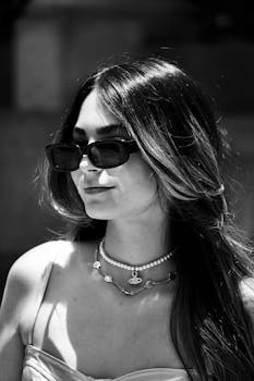 Elegant woman wearing sunglasses and jewelry in a black and white close-up shot.