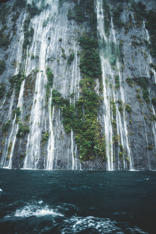Free Vertical shot of waterfalls flowing down lush, rocky cliffs amidst a serene nature setting. Stock Photo