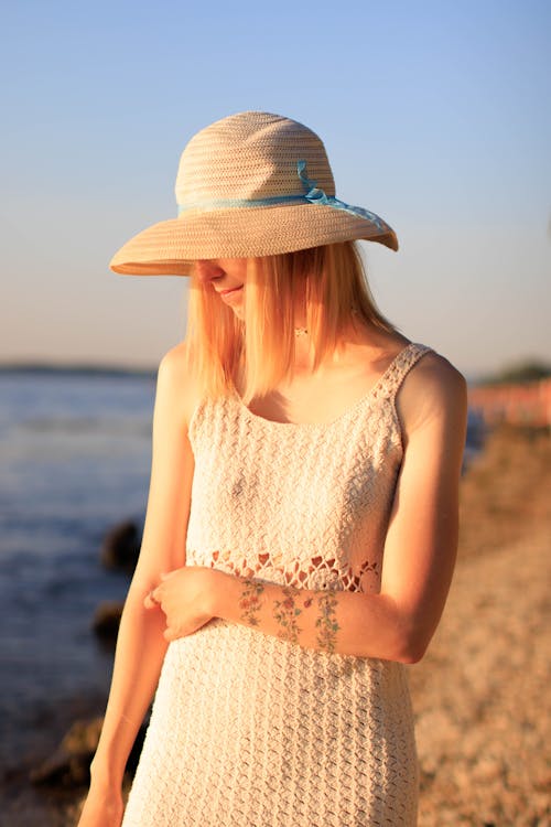 A Woman in White Sleeveless Crochet Dress and Sun Hat Standing on Beach