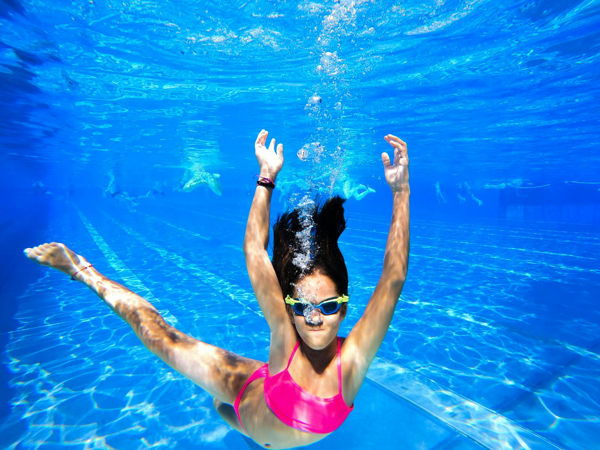 Woman enjoying underwater swimming in a vibrant blue pool wearing goggles and swimwear.