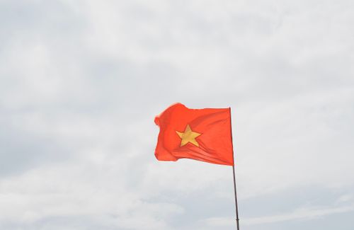 Free Bright red Vietnamese flag with a yellow star waving against a cloudy sky. Stock Photo