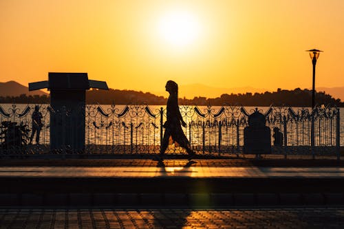 A Woman Walking on Sidewalk During Sunset