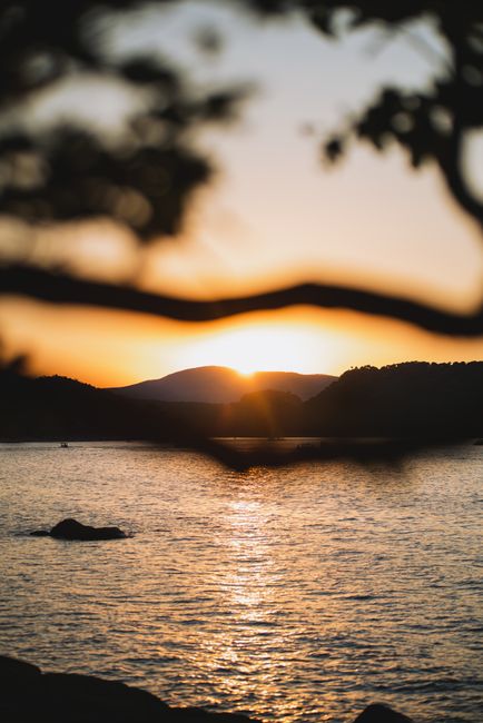 Peaceful sunset scene over a calm lake with mountain silhouettes in the background.