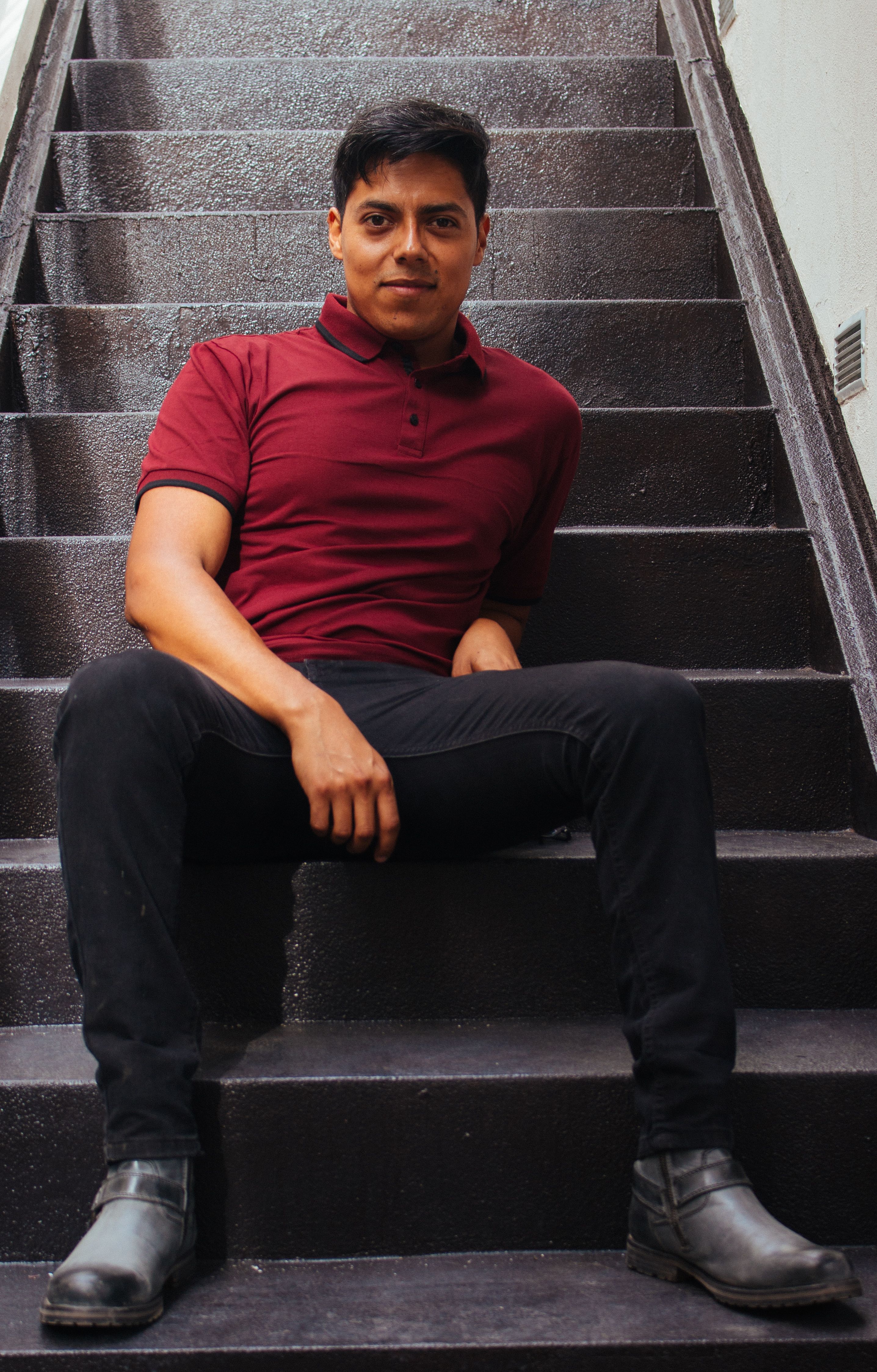 Portrait of a young man in a burgundy polo shirt sitting on stairs.