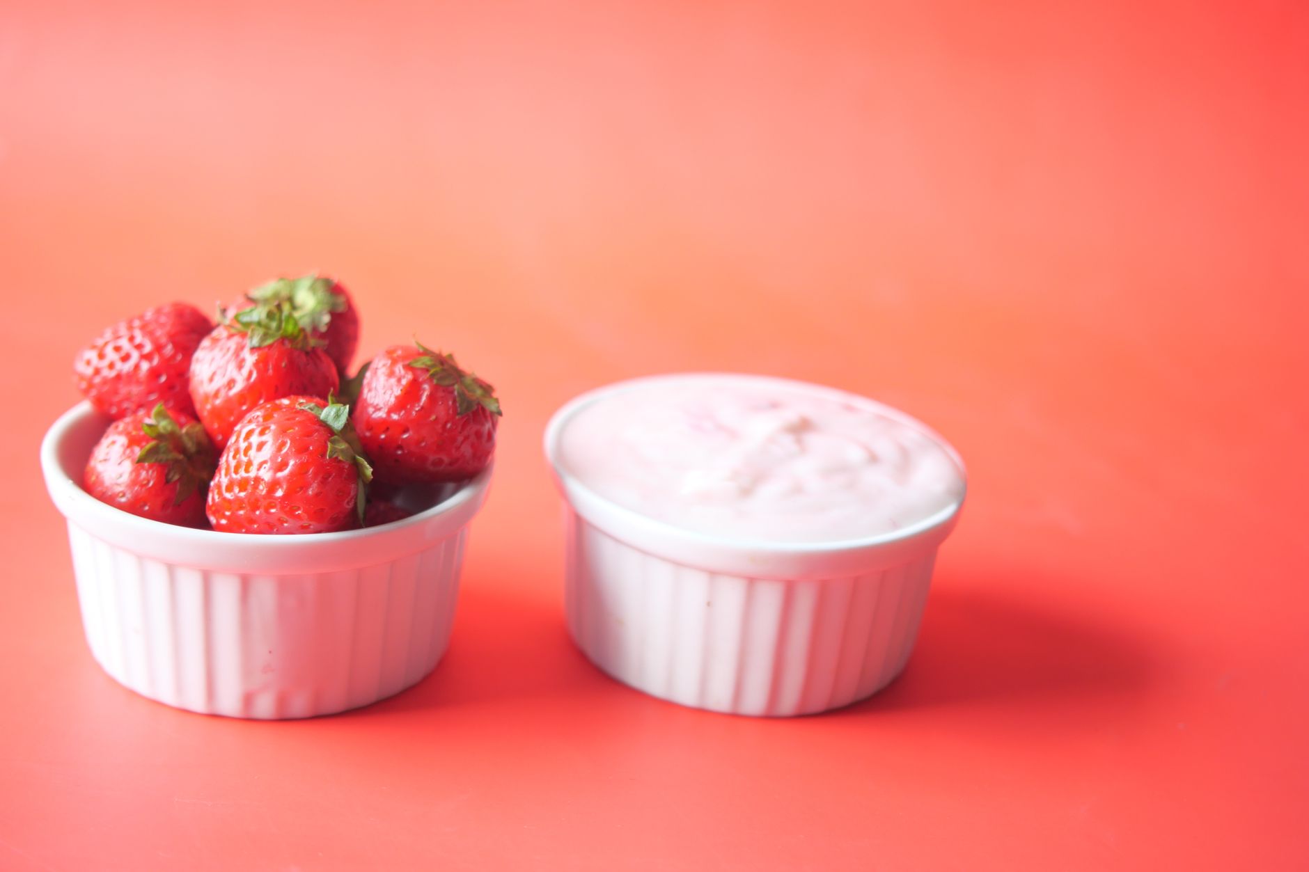 地中海飲食也能吃甜點:低糖健康食譜分享 A bowl of fresh strawberries and creamy yogurt on a vibrant orange background.