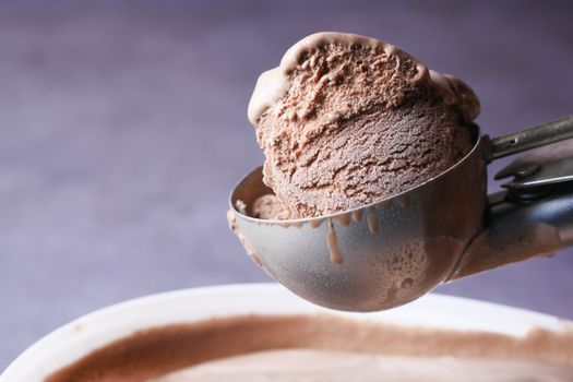 Delicious chocolate ice cream scoop in metal scooper against a neutral background.
