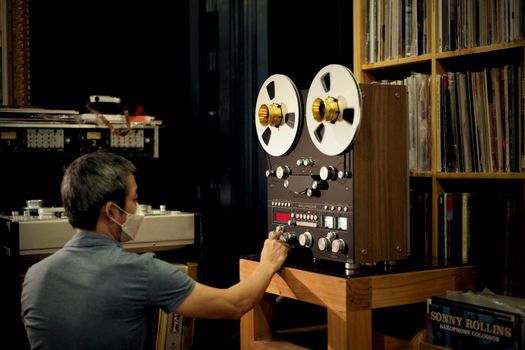 A man adjusting a vintage reel-to-reel tape recorder in a library setting, focusing on analog sound technology.