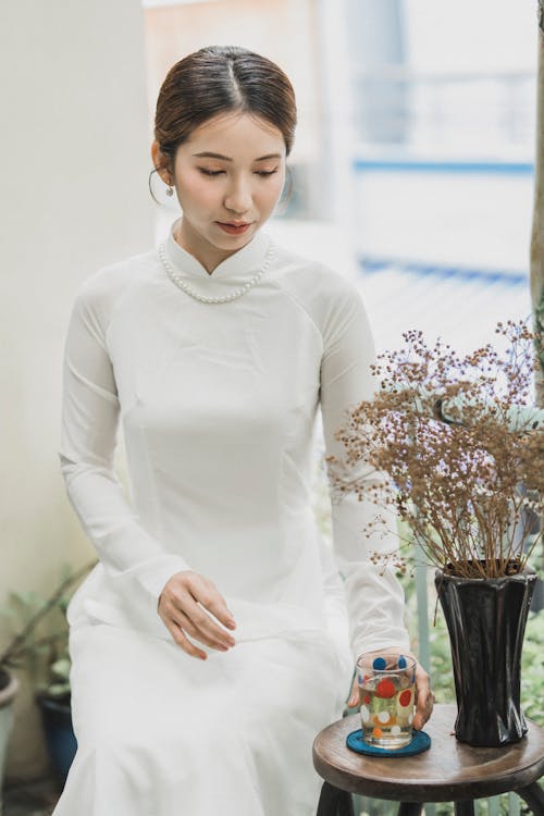 Free A Woman in a White Dress Sitting Near a Vase Stock Photo