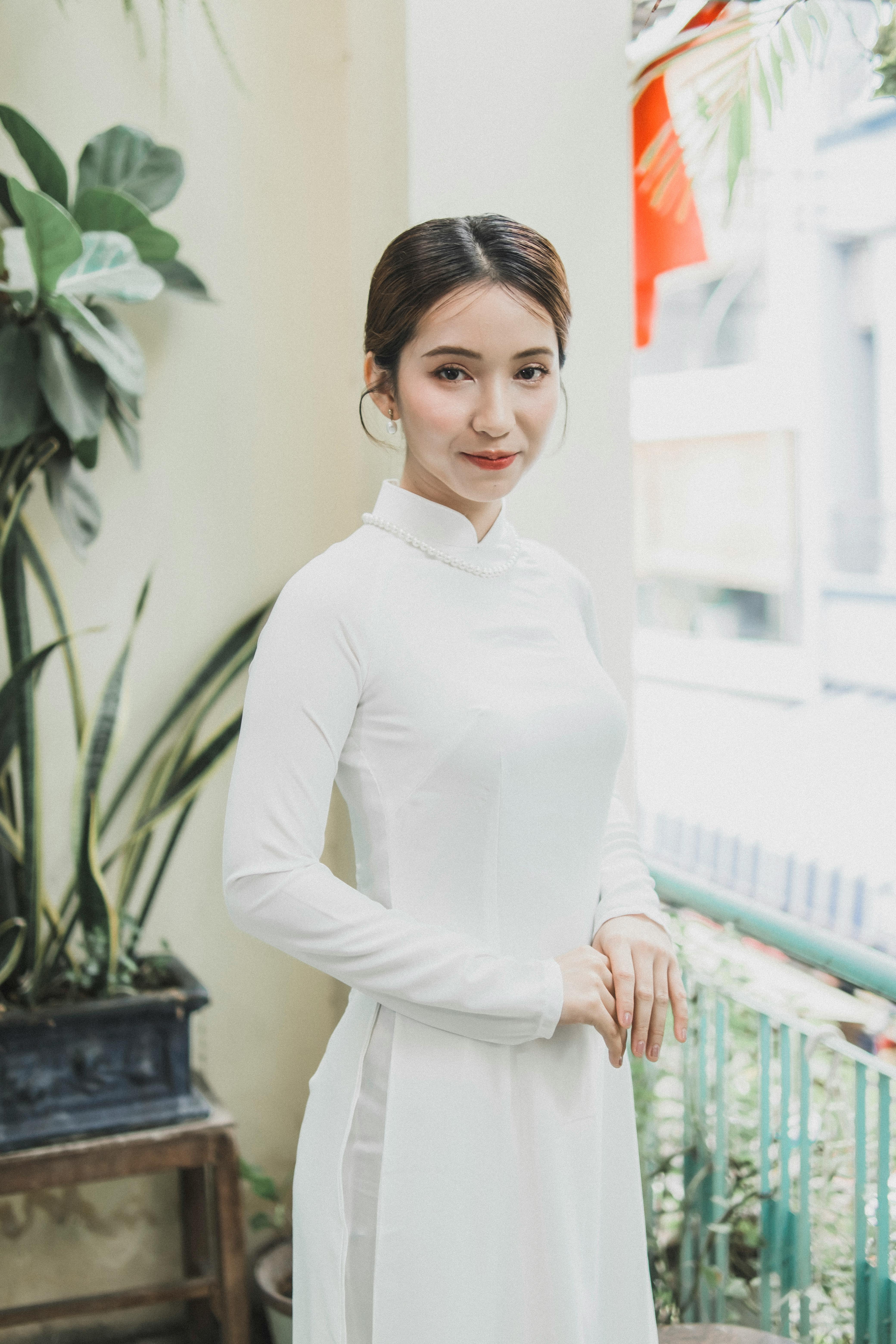 A woman in a white Ao Dai, standing indoors, exuding grace and elegance.