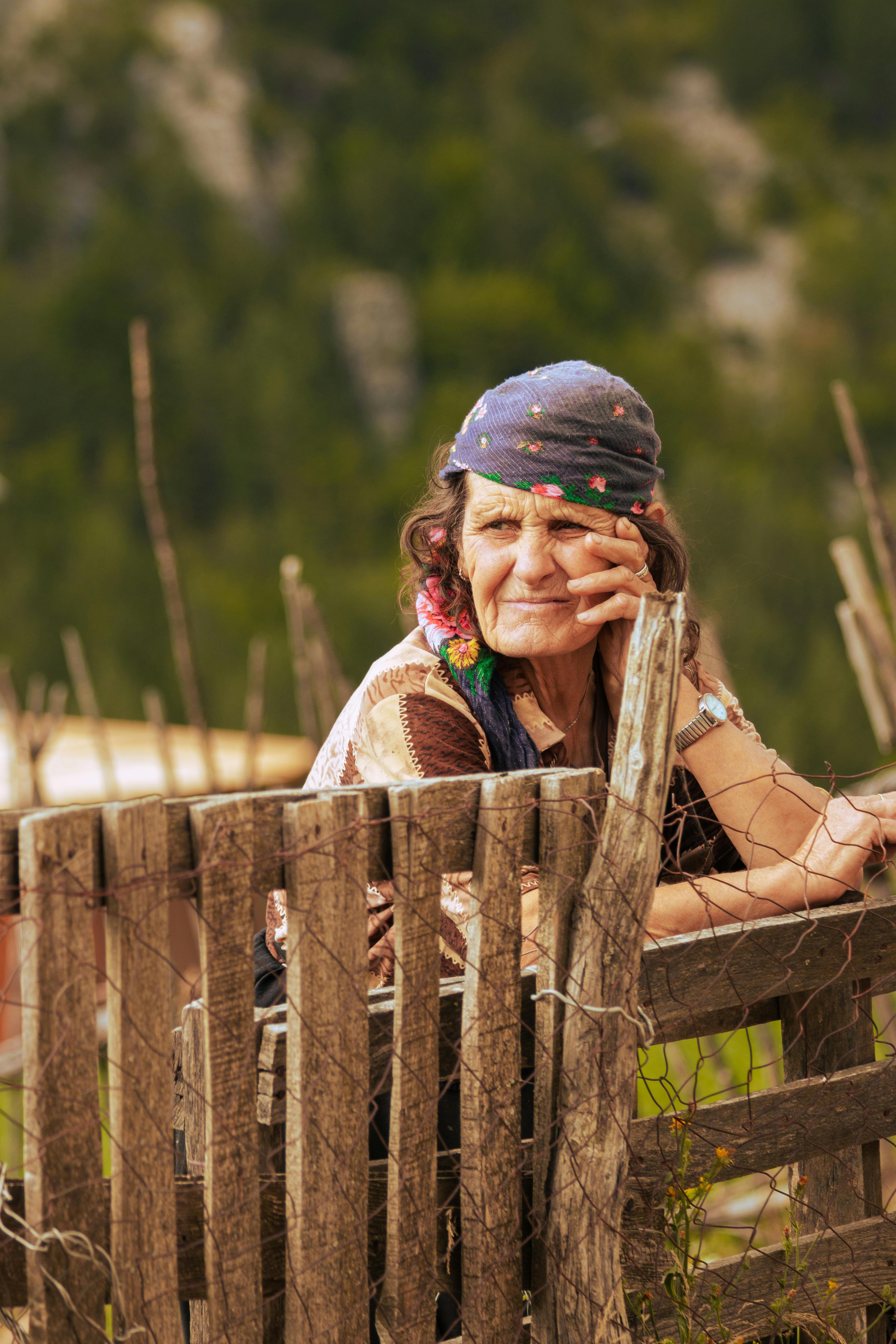 Elderly woman resting by a wooden fence in rural Theth, Albania, showcasing traditional culture.